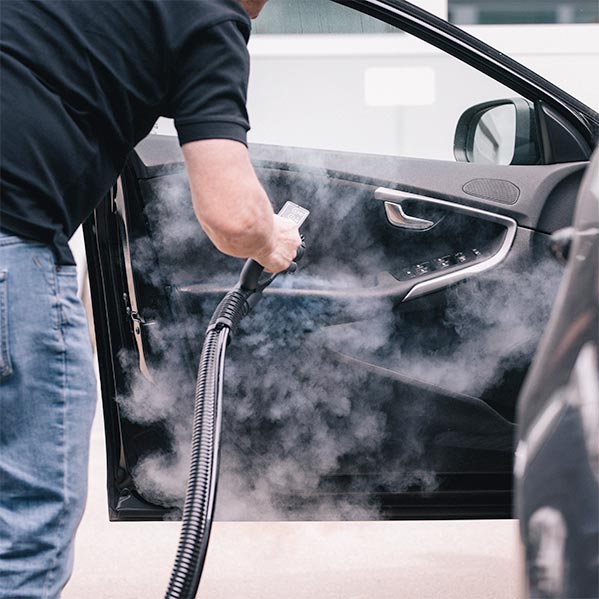 Un professionnel du nettoyage automobile nettoie l'intérieur d'une porte de voiture à la vapeur.