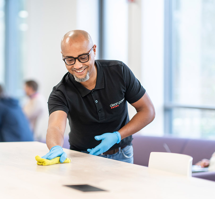 Professionnel du nettoyage utilise un chiffon pour nettoyer un bureau dans un espace de coworking.