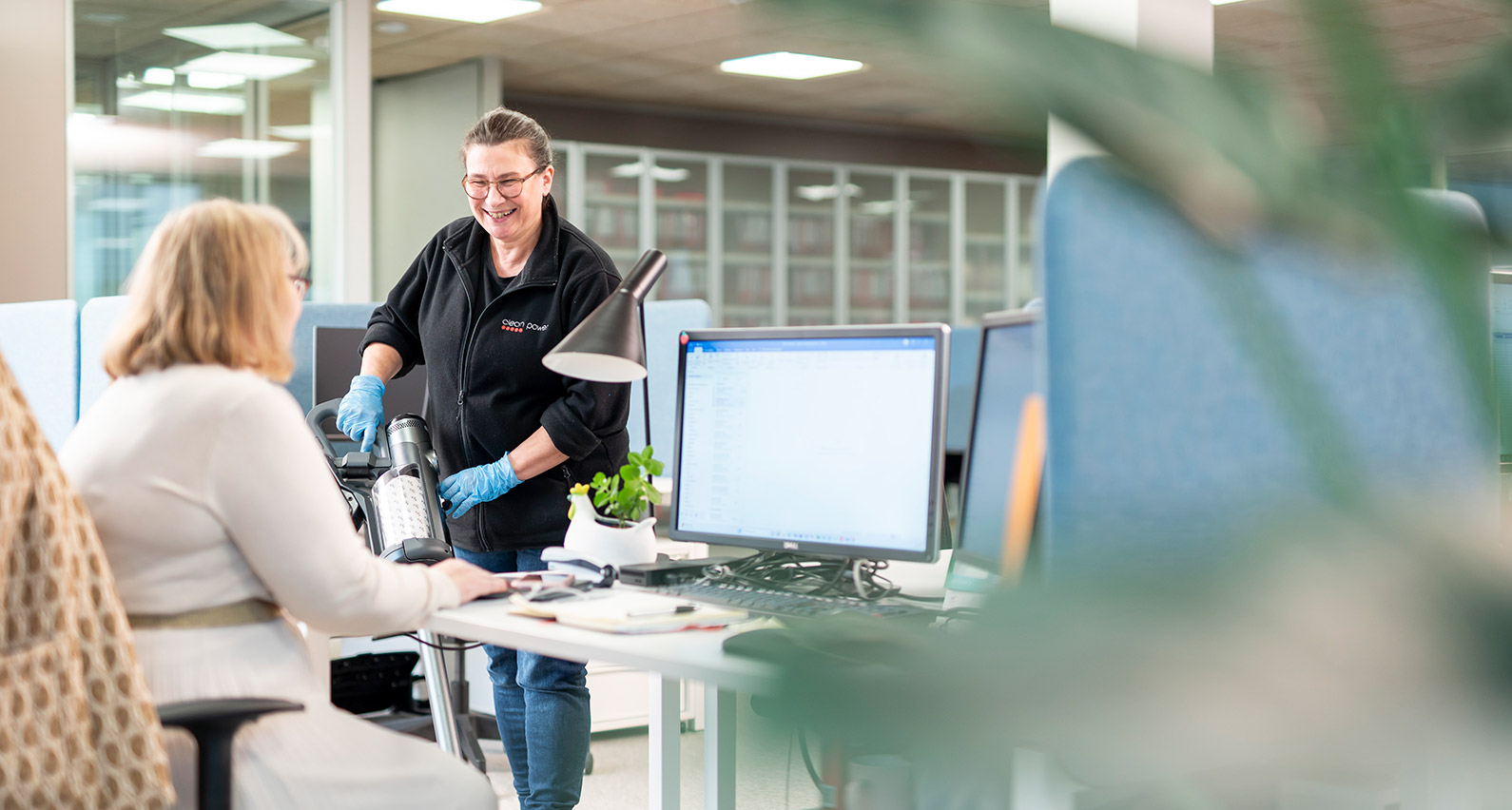 Femme professionnel du nettoyage en train d’aspirer entre des bureaux.