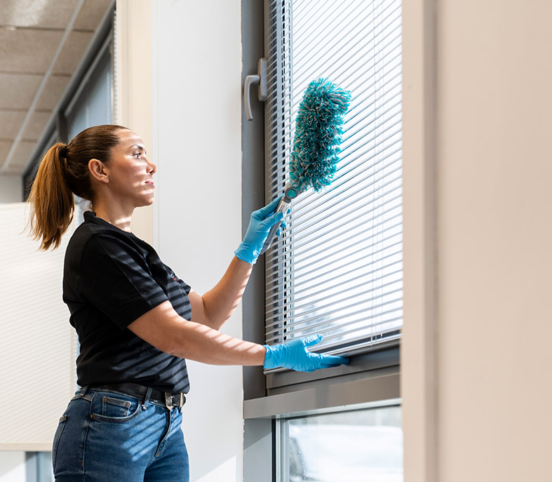 Femme faisant les poussières d'une persienne dans un bureau.