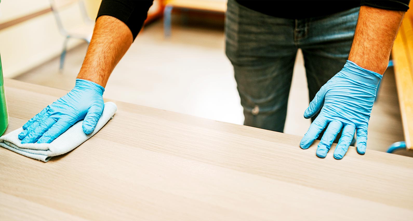 Mains équipées de gants hygiéniques qui nettoient un banc d’école.