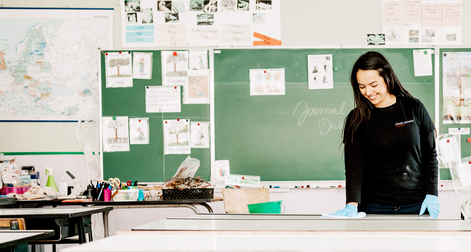 Femme souriante en train de nettoyer un banc dans une classe d’école.
