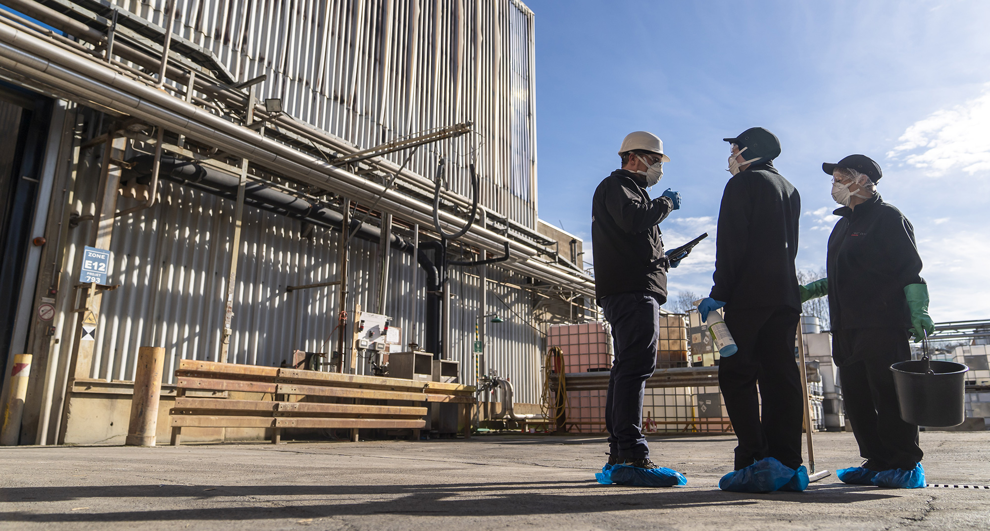 Techniciens industriels qui écoutent les consignes d’hygiène et de nettoyage devant une usine.