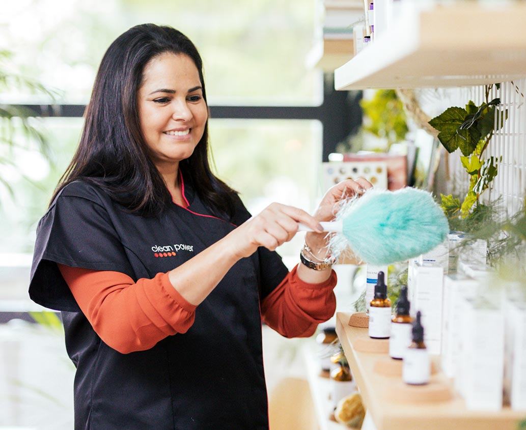 Femme souriante en train de nettoyer les étagères d'un magasin.