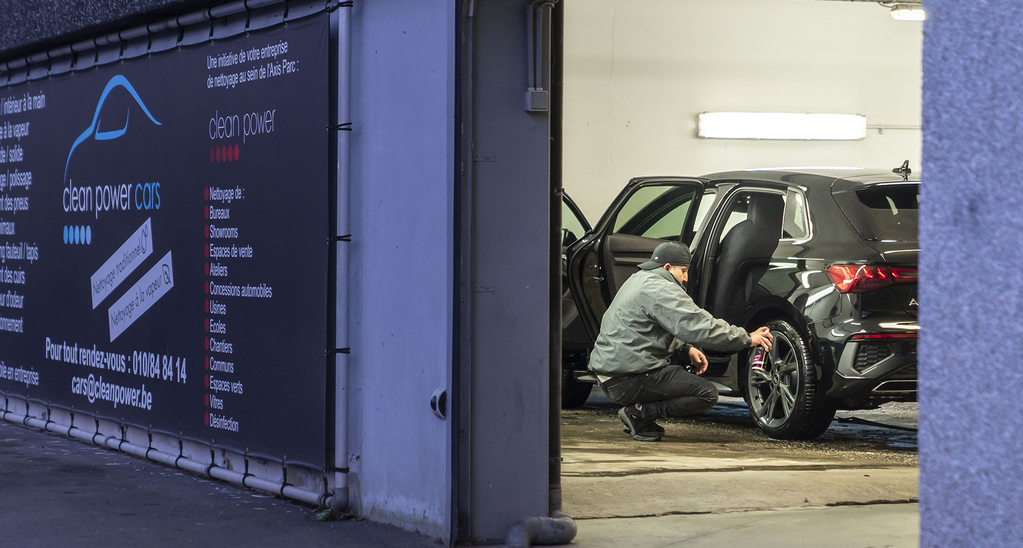 Homme nettoyant les jantes d'une voiture sur un parking.