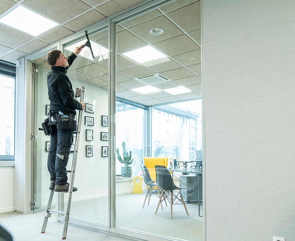 Professionnel sur une échelle en train de laver une vitre dans un bureau.