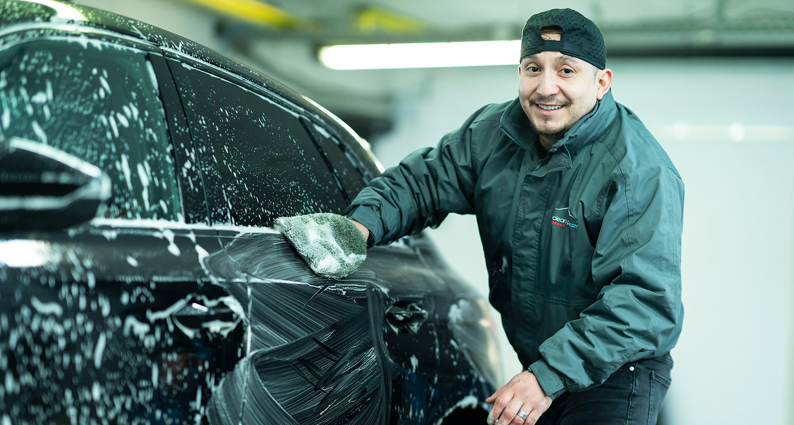 Technicien Clean Power en train de nettoyer une voiture avec du savon sur un parking.
