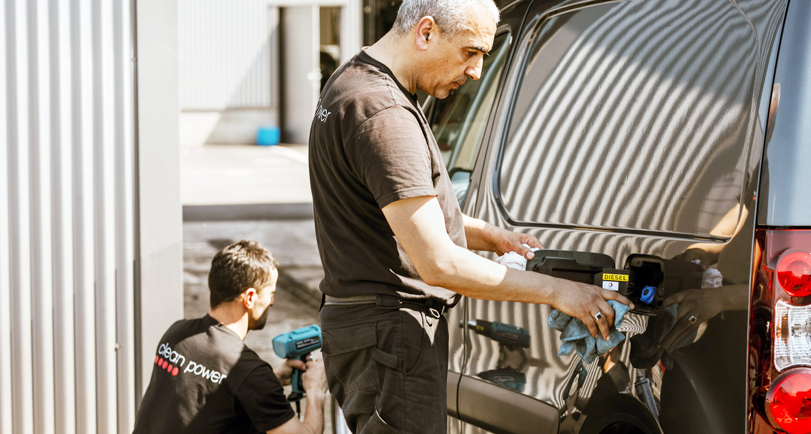 Deux professionnels nettoient une voiture sur un parking.